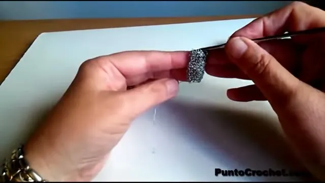 Tubo de malla de alambre plateado montado sobre la aguja de crochet, sostenido con los dedos