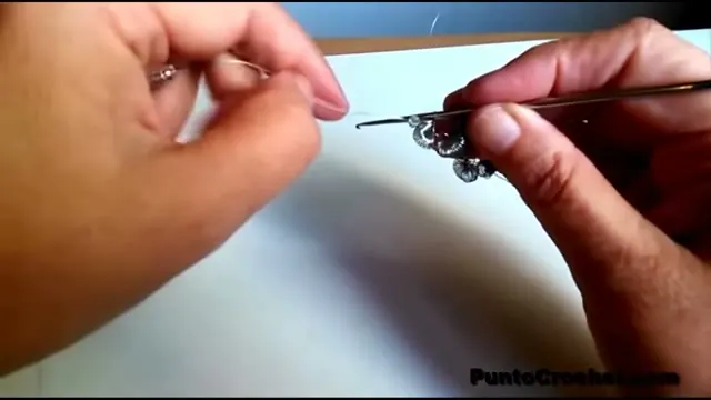 Aguja de crochet trabajando en el último rulo de la tira, con el hilo largo a un costado