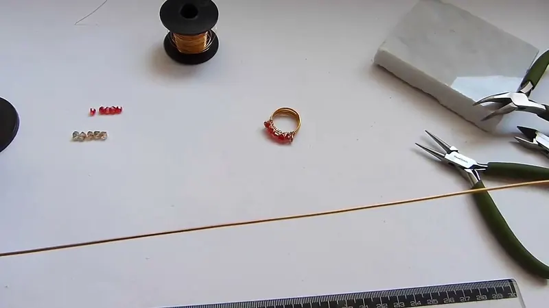 Alambre dorado largo estirado sobre la mesa junto a una regla, con cristales y pinzas de fondo