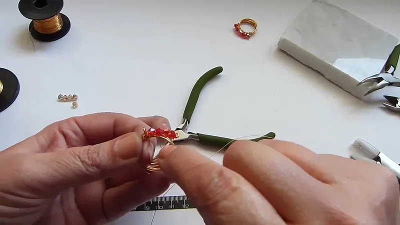Pinza de punta plana apoyada en la banda de alambre con los cristales rojos enhebrados
