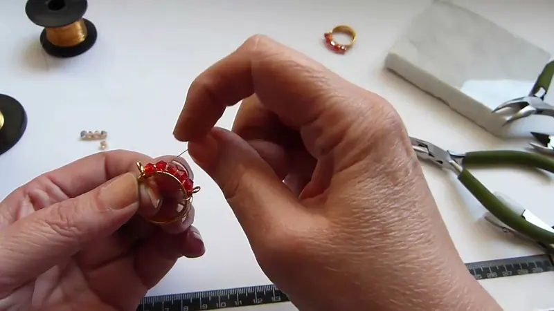 Manos que pasan el alambre fino entre los cristales rojos para formar la B