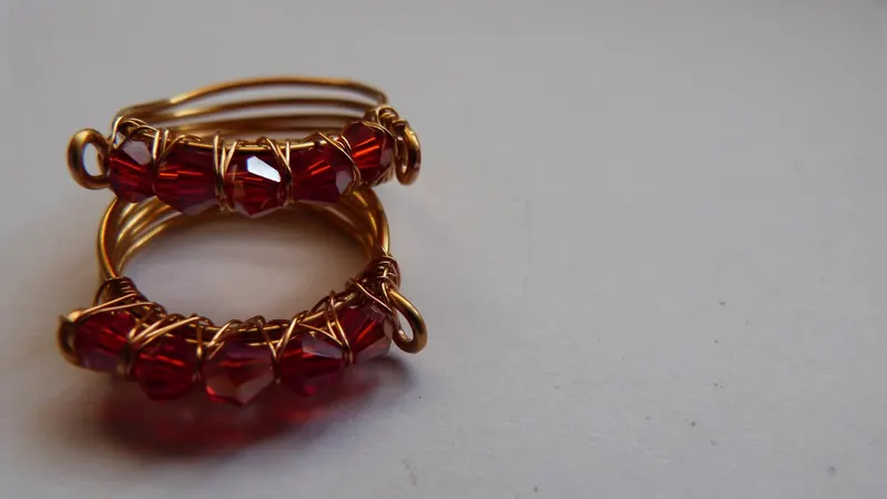 Dos anillos cintillo de alambre dorado con cinco cristales rojos cada uno y un aro en cada extremo