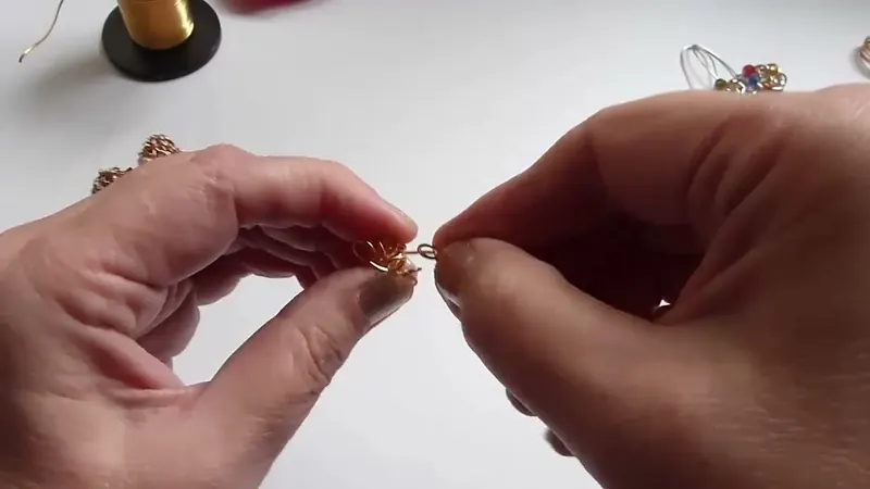 Las dos manos armando con los dedos una pequeña bola de aros de alambre dorado