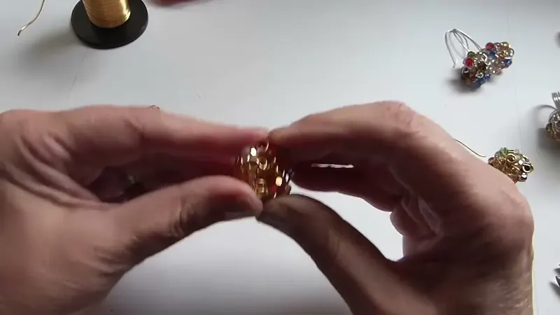 Las manos sosteniendo una esfera de alambre dorado con cristales, redondeándola con las palmas