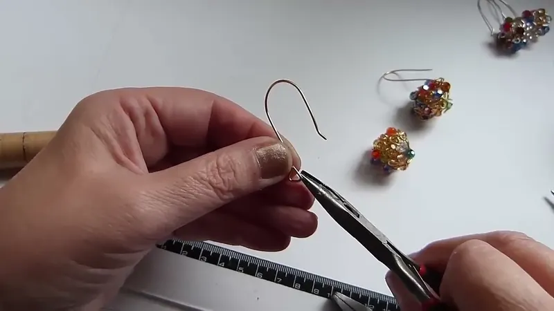 Una pinza plana doblando el gancho, junto a una esfera de alambre y cristales apoyada en la mesa