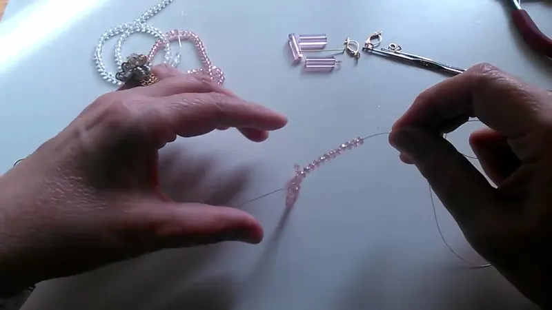 Una hilera de cristales rosados enhebrada en un alambre fino sobre la mesa, con las manos alrededor