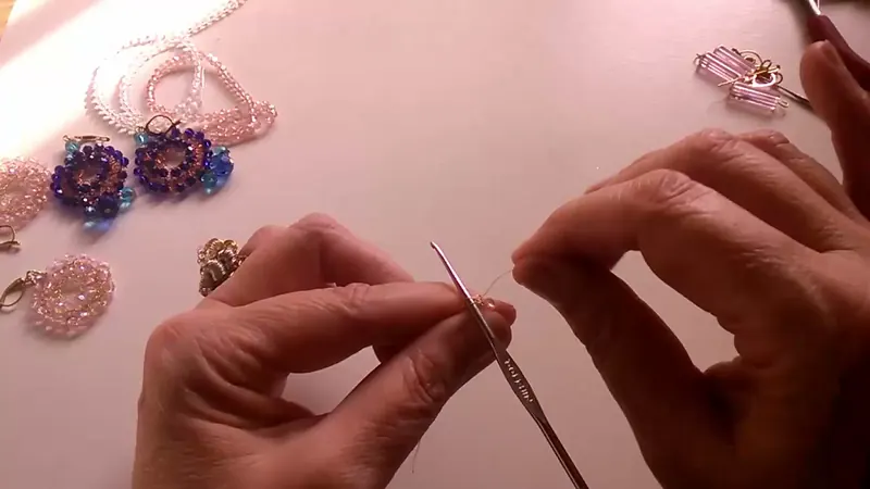 La aguja de crochet sostenida entre los dedos con el alambre pasando por debajo mientras se desliza un cristal