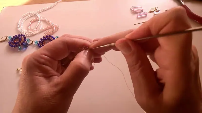 Las manos con la aguja de crochet fina tomando un punto bajo del aro de cristales