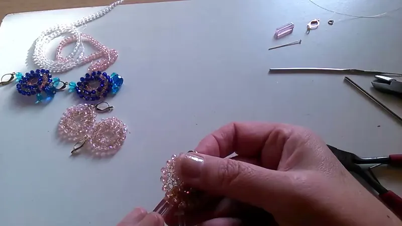 Las manos sujetando el aro de cristales con el adorno de tubitos rosados colgando y una pinza al costado