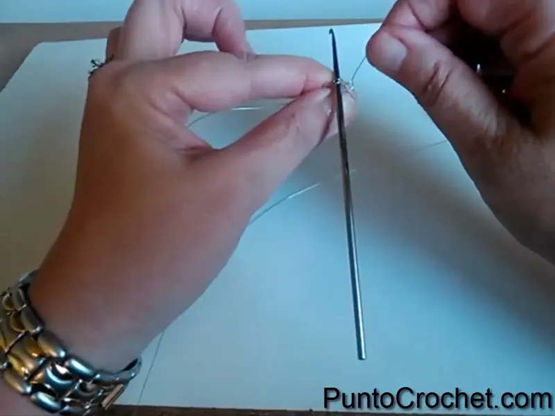 La aguja de crochet apoyada en el aro de alambre, sostenido entre los dedos, al armar la cadeneta