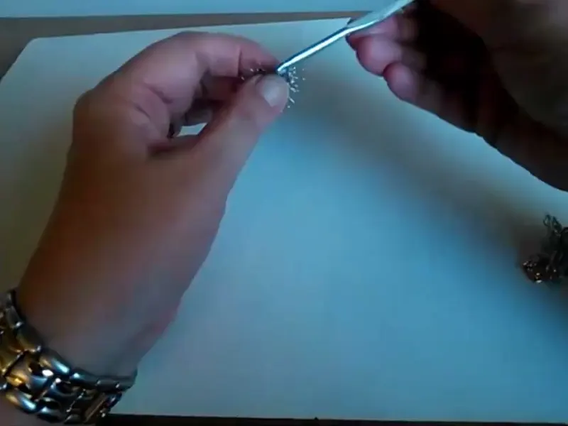 La aguja de crochet de aluminio, azulada, trabajando sobre la rueda de malla