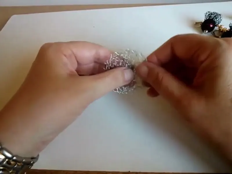 Las dos manos sostienen la malla de alambre ya terminada, levantada para ver la trama