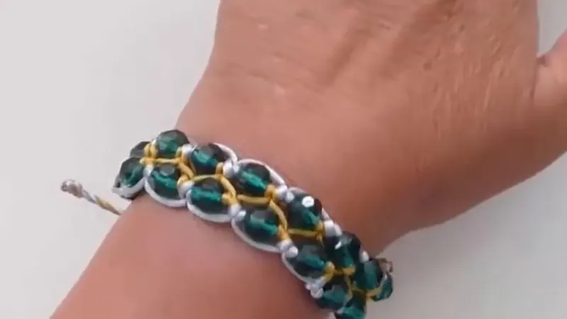Pulsera de macramé con cristales verdes y cordón blanco y dorado, puesta en la muñeca