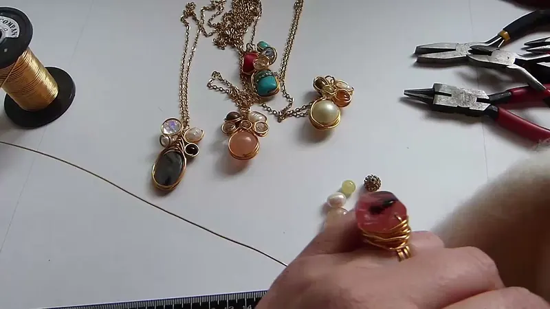 El alambre dorado sobre la mesa mientras se lo alisa con un paño, junto a las gemas elegidas