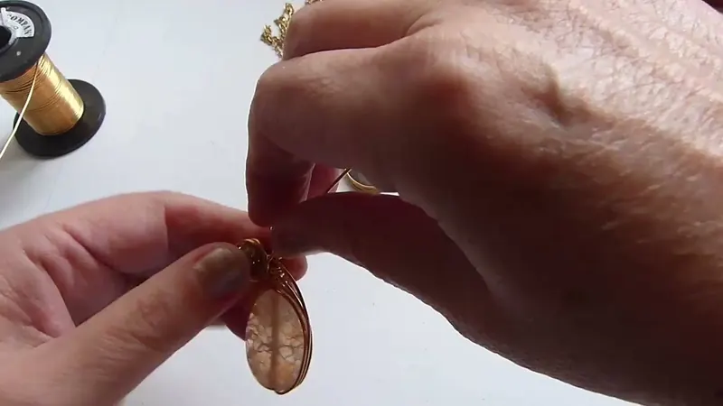 Las manos sujetando la piedra ovalada mientras el alambre rodea la cuenta de arriba