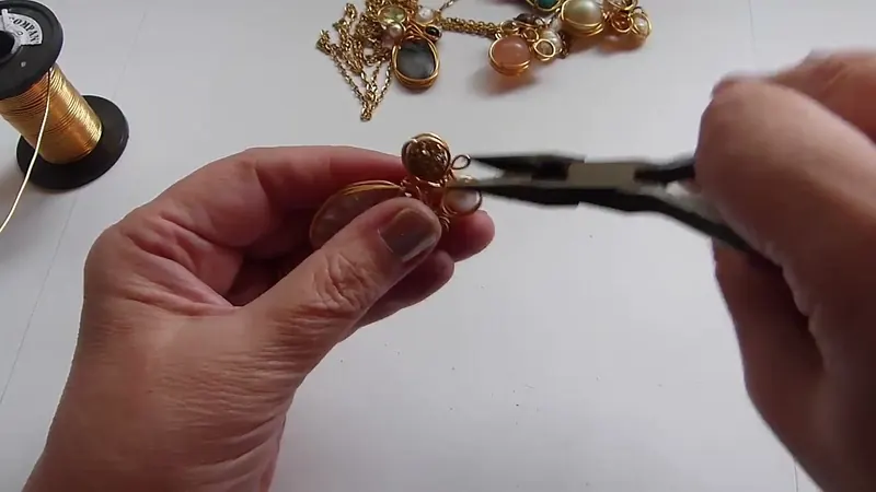 Una pinza junto al colgante ya armado, acomodando el alambre sobrante