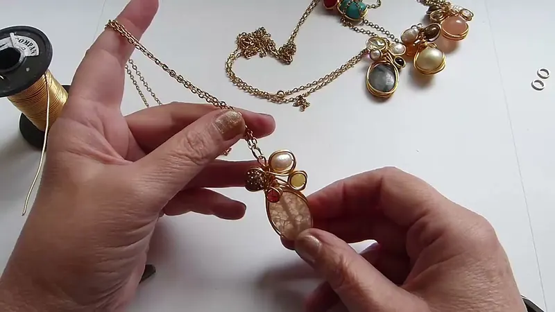 Colgante de alambre dorado con una piedra ovalada, una perla y cuentas chicas, colgado de una cadena
