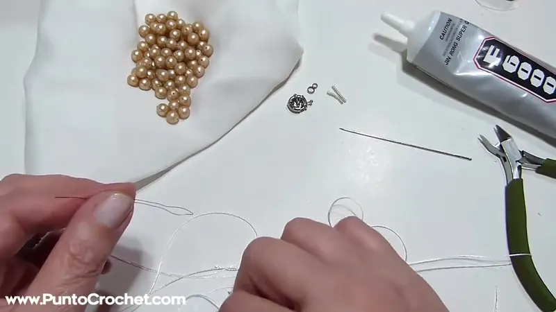 Las manos enhebran la aguja de alambre fino con el hilo, con las perlas, el cierre y las pinzas sobre la mesa
