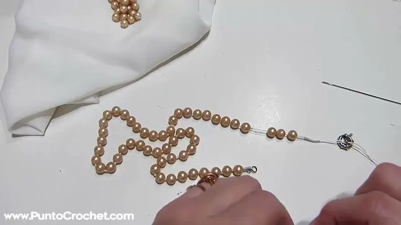 El collar largo de perlas enfiladas sobre la mesa, con las últimas perlas y la segunda parte del cierre en el extremo del hilo