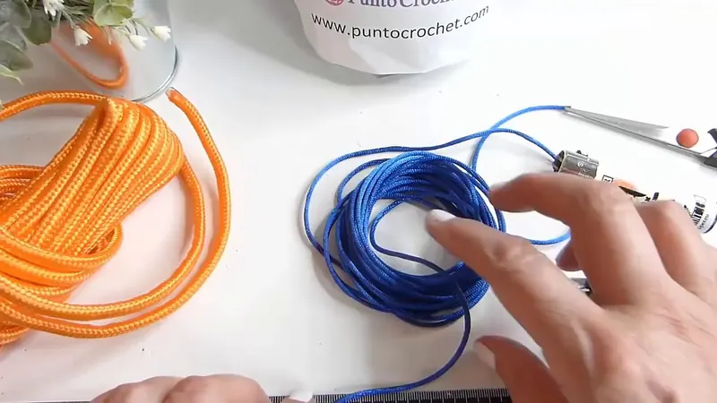 Soga de paracord naranja enrollada junto a un cordón de seda azul, un mechero, alicates y una regla