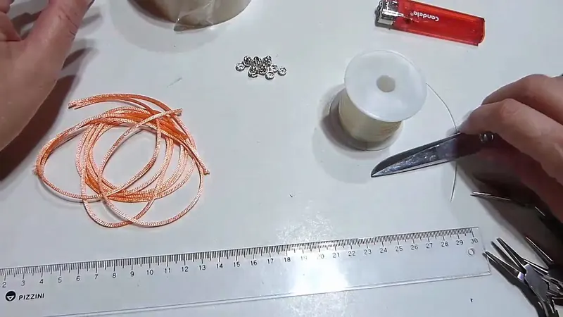 Cordón de seda naranja enrollado, tijeras, anillas y un carrete de tanza elástica sobre la mesa