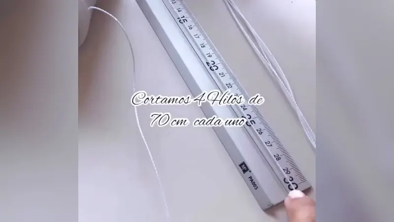 Hilos blancos estirados junto a una regla, con el cartel «Cortamos 4 hilos de 70 cm cada uno»