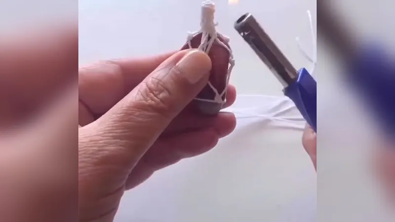 Gema roja envuelta en una red de hilo blanco, con un tallo de nudos arriba, sostenida entre los dedos