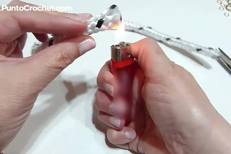 Una mano sostiene el extremo de una cuerda blanca de nailon sobre la llama de un encendedor rojo que sujeta la otra mano