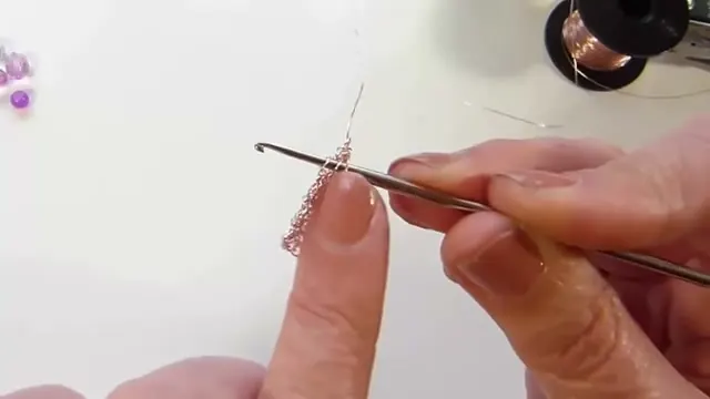 Aguja de crochet enganchada en la malla de oro rosa mientras se hace la disminución