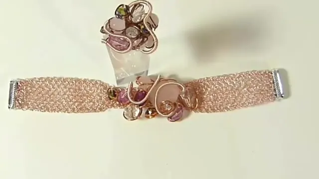 Brazalete de malla de alambre color oro rosa con un adorno central de gemas y terminales plateadas, junto a un anillo con el mismo estilo