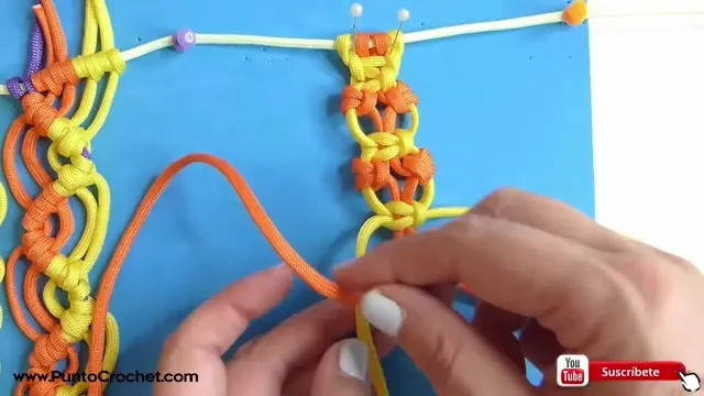 Columna naranja y amarilla del nudo japonés con una mano sosteniendo la soga naranja para el siguiente nudo