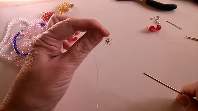 Flor central de seis pétalos de alambre sostenida entre los dedos, con la aguja de crochet a un lado