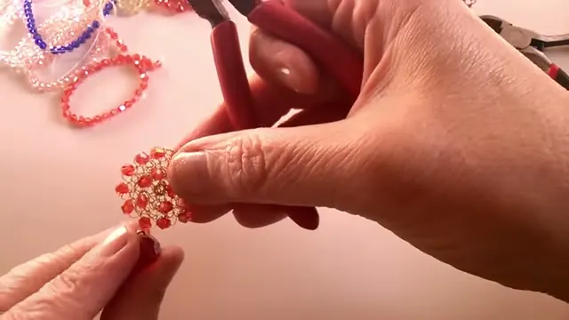 Mano con la pinza y la pieza tejida, con un cristal rojo colgando en la base