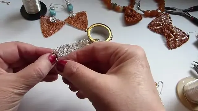 Las manos sostienen el borde del triángulo de malla mientras pasan el alambre sobrante por los aros del costado