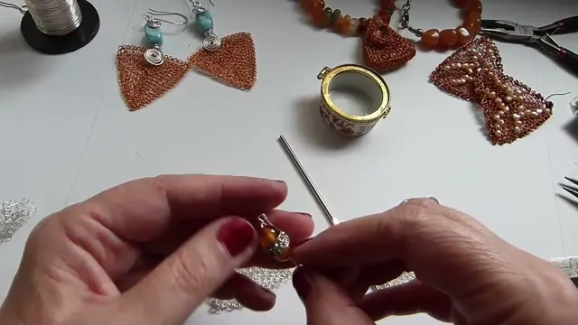 Manos sosteniendo el sostén de alambre con la gema, los strass y la segunda gema ya colocados
