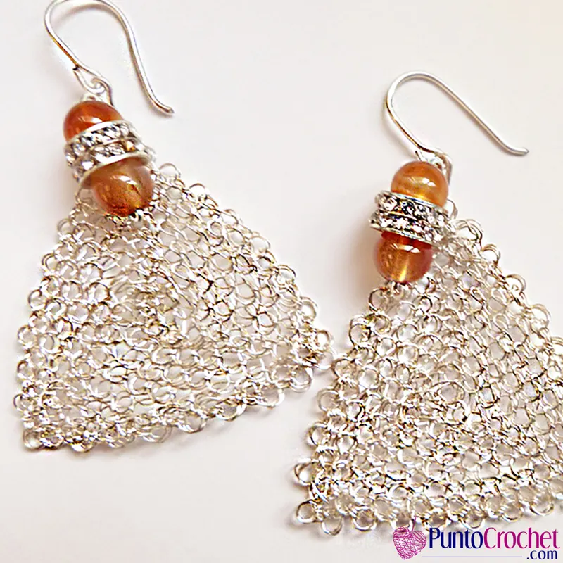 Par de pendientes triangulares de malla de alambre color plata, con dos cuentas anaranjadas y un rondel de strass arriba, colgados de ganchos