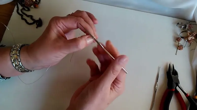 Aguja de crochet con el alambre montado mientras la otra mano sostiene los aros de la cadeneta
