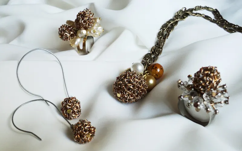 Aros con una esfera tejida en alambre colgando de cada gancho, junto a un anillo y un colgante con esferas del mismo tejido