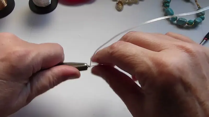 La pinza de punta plana sujetando el aro mientras la otra mano enrolla el alambre