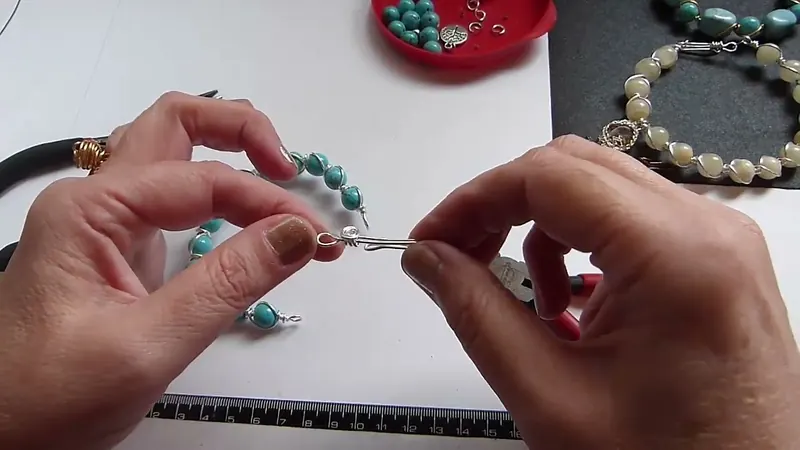 Las manos uniendo el cierre de gancho con el extremo de la pulsera, con una pinza a un costado