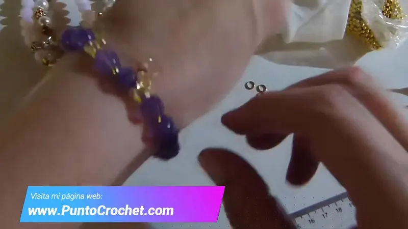 La pulsera de amatistas puesta en la muñeca, con el colgante dorado al lado