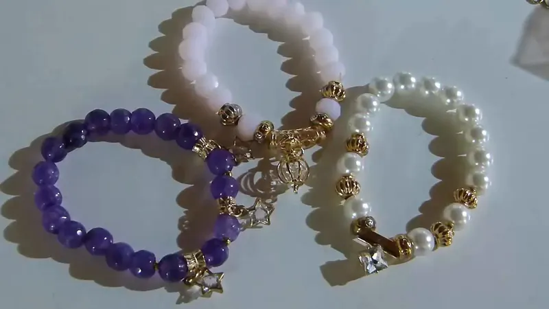 Tres pulseras elásticas con cuentas: una de amatistas violetas con colgante, una de cuarzo rosa y una de perlas blancas