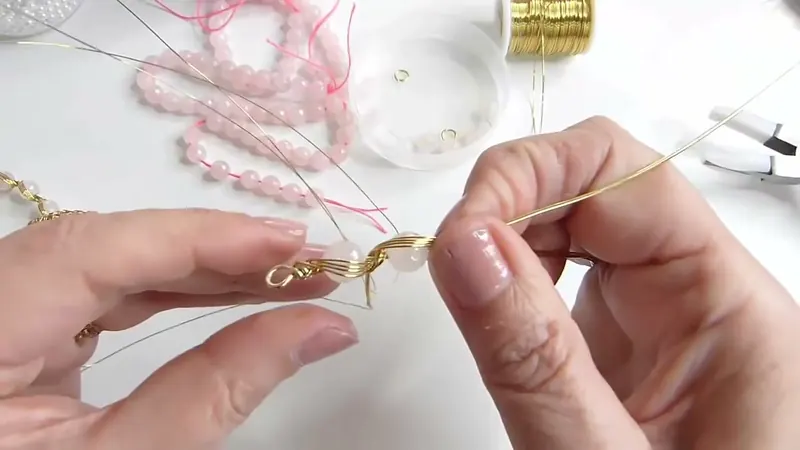 Las manos sujetando la primera gema de cuarzo rosa sobre el eje, con los alambres torcidos a los costados