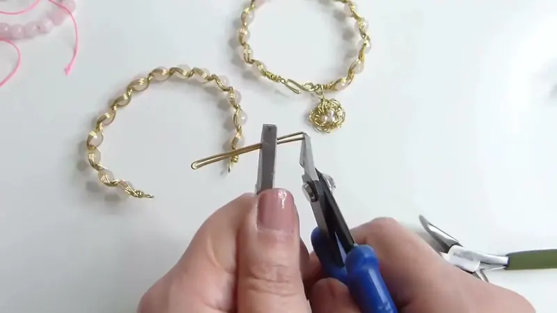 Dos pinzas doblando un alambre dorado para el broche, con la pulsera curvada al fondo