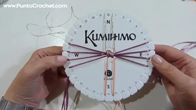Disco kumihimo con doce hilos: ocho morados a los lados, dos rosas abajo y dos dorados arriba