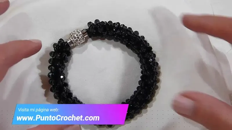 Brazalete kumihimo de cristales negros facetados con un cierre magnético de pedrería, entre las manos de Adriana