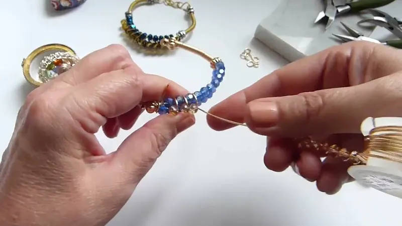 Las manos pasan el alambre entre los cristales azules mientras acomodan uno claro en el medio