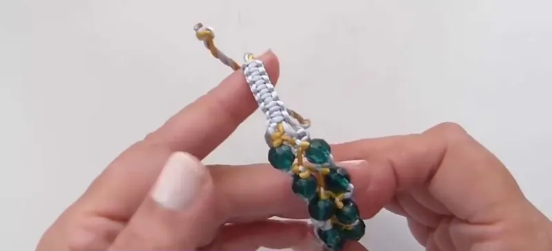 Pulsera de macramé en cordón plateado y dorado con cuentas verdes de cristal, sostenida entre las dos manos