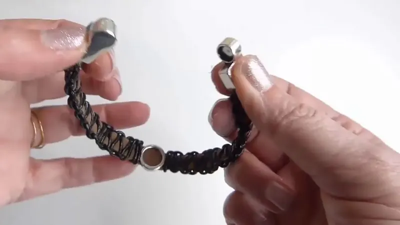 Pulsera negra de cuero y gamuza con cierre de imán plateado, que una mano abre por la mitad