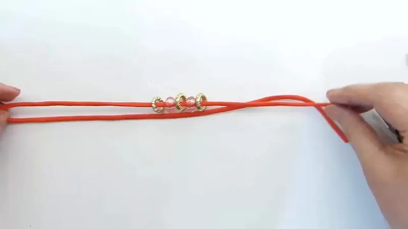 Una soga naranja doblada al medio con dos abalorios rosas y tres arandelas doradas enhebrados en el centro